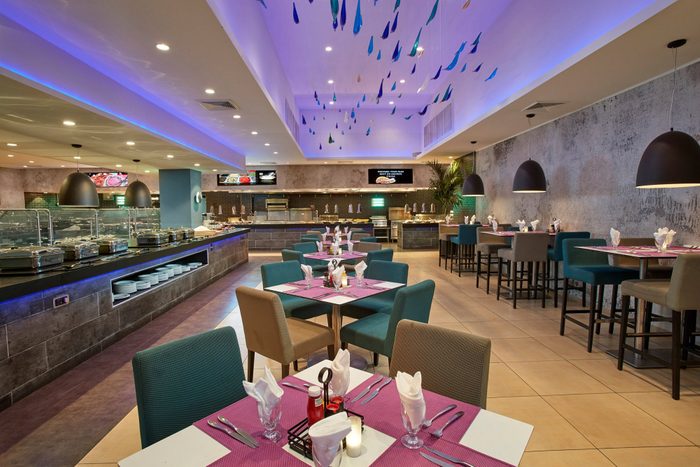 Tables set for dining in a modern, stylish restaurant with colorful ceiling decor and a buffet in the background.