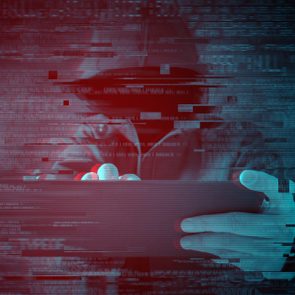 Hooded figure types on tablet, surrounded by glitching digital effects in a dark, red-blue toned environment.