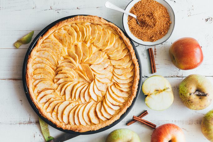 Freshly baked apple pie tart with custard filling on a rustic white wooden background