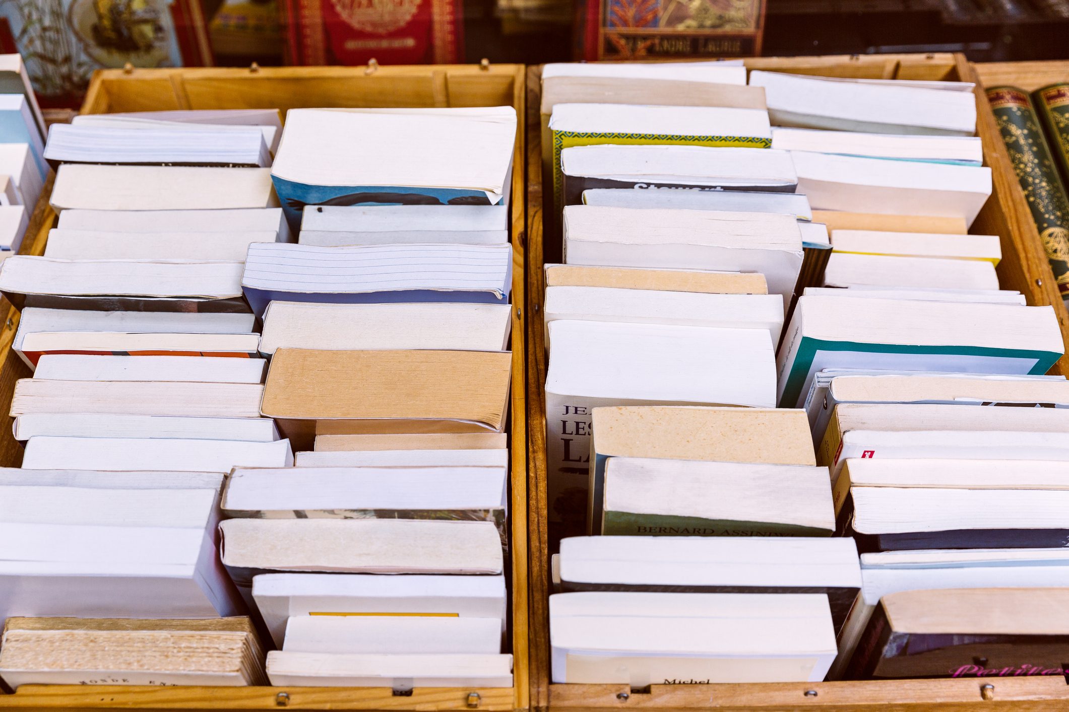 Books stacked vertically, showing spines, within wooden boxes on a shelf.