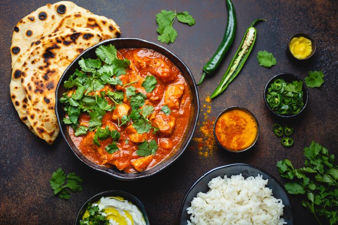 Traditional Indian dish Chicken tikka masala with spicy curry meat in bowl, basmati rice, bread naan, yoghurt raita sauce on rustic dark background
