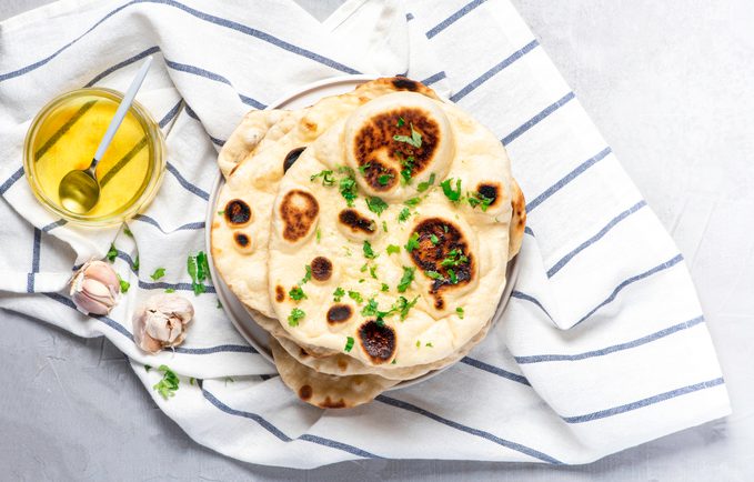 Traditional Indian garlic naan bread with butter and parsley on a white towel, top view