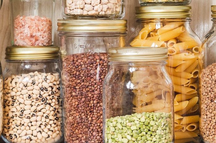 Shelf in the kitchen with various cereals and seeds - peas split, sunflower and pumpkin seeds, beans, rice, pasta, oatmeal, couscous, lentils, bulgur in glass jars