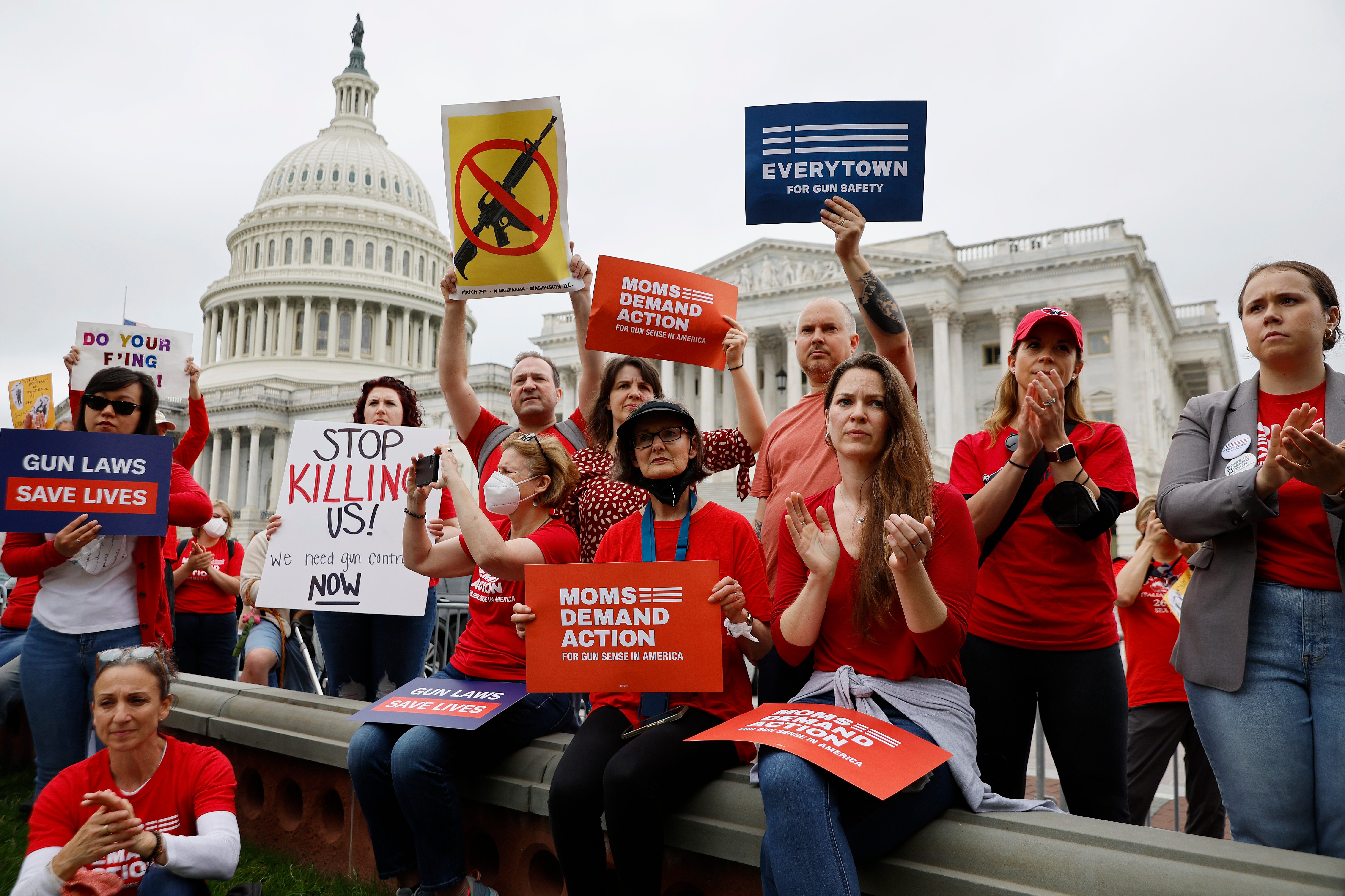 Protesters hold signs advocating for gun control, standing together near the U.S. Capitol building, wearing red shirts and appearing focused and intent.