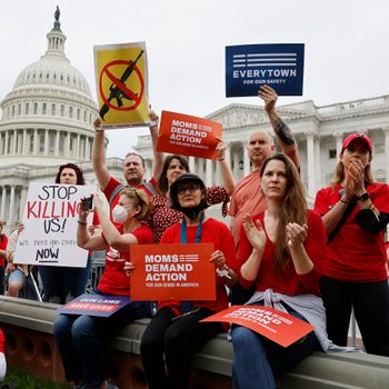 Protesters hold signs advocating for gun control, standing together near the U.S. Capitol building, wearing red shirts and appearing focused and intent.