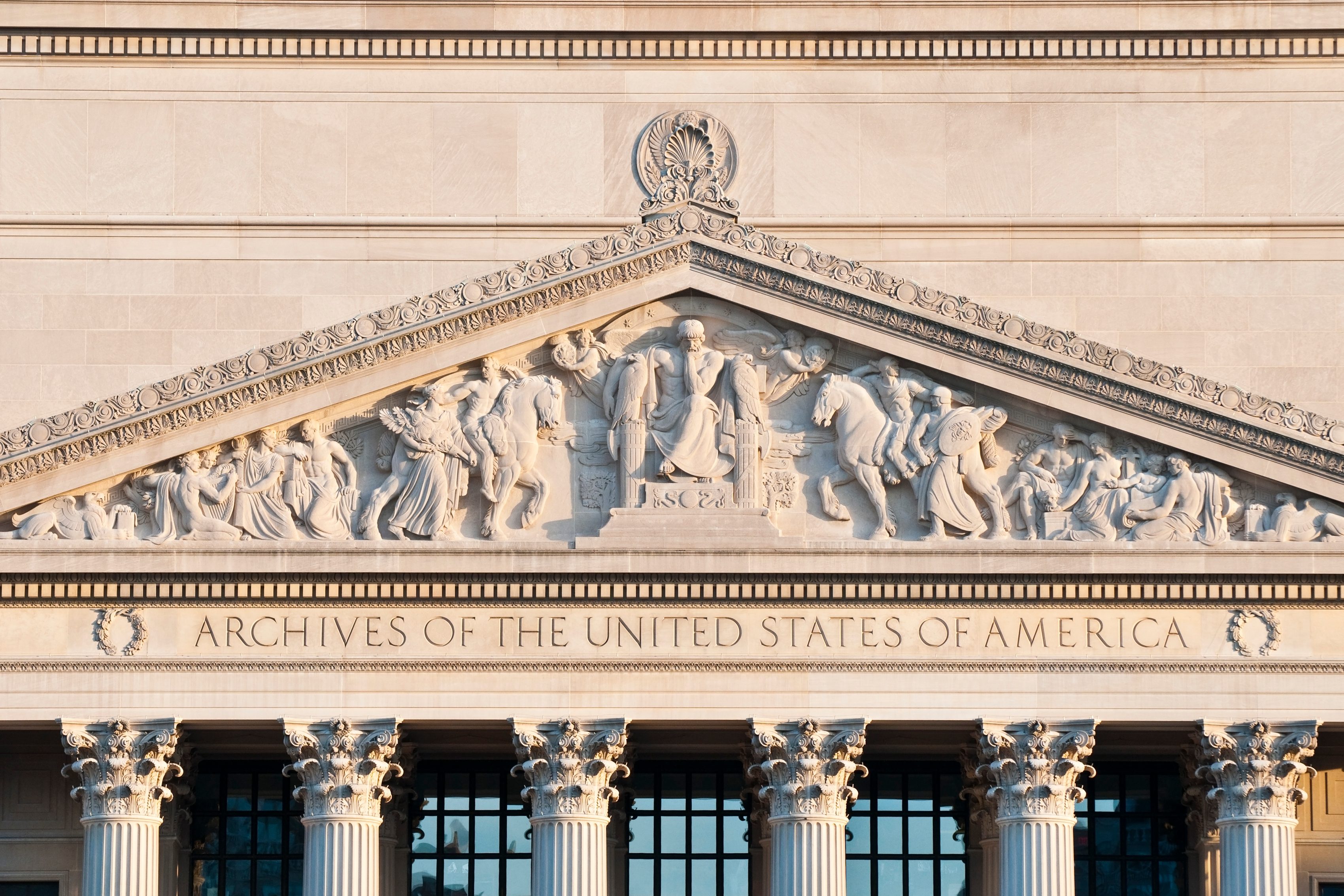 Pediment sculpture displays seated figures and horses, symbolizing historical themes. Below, text reads "ARCHIVES OF THE UNITED STATES OF AMERICA" on a classical building facade.