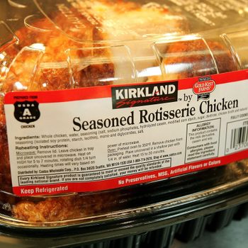 Rotisserie chicken sits in a clear plastic container labeled "Kirkland Seasoned Rotisserie Chicken," with ingredient and reheating instructions.