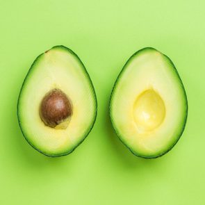 Two avocado halves rest on a vibrant green background, one with a seed, the other without.
