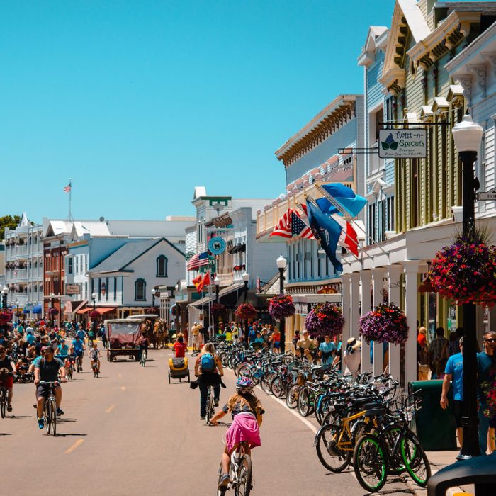Bicycles crowd the lively street, with colorful shops and flags lining the bustling town atmosphere.
