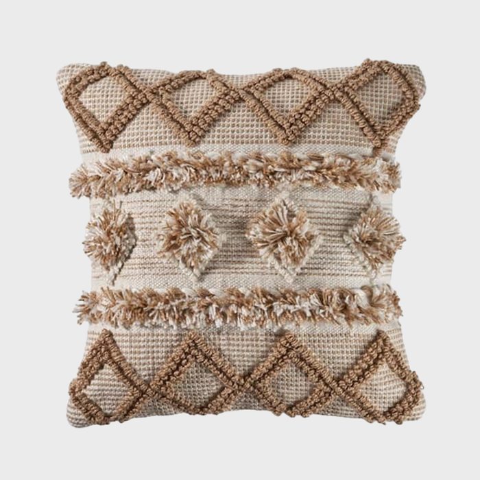 Square decorative pillow featuring textured geometric patterns and fringes on a woven beige fabric background, creating a cozy, bohemian feel.