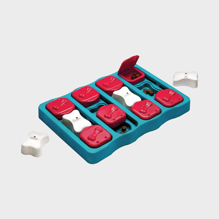 Puzzle toy holds treats in small compartments, some with red lids open, surrounded by white and red bones, set on a gray background.