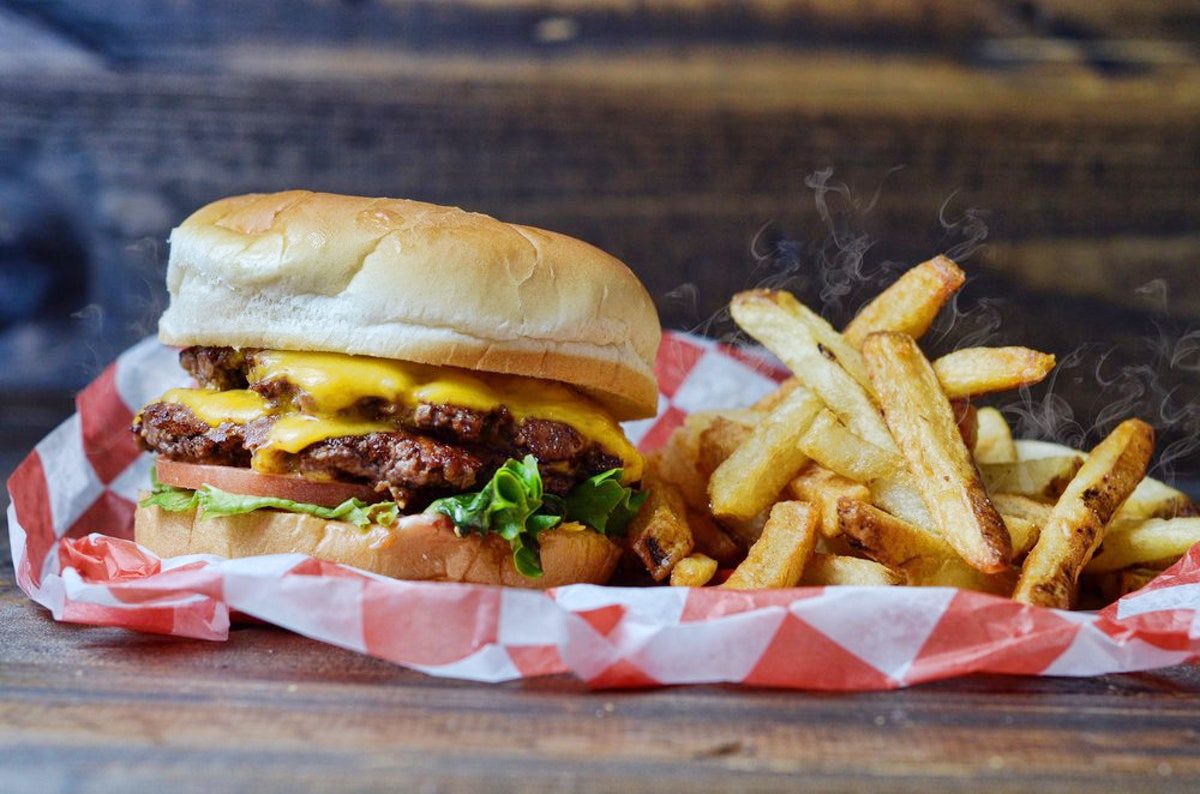 A cheeseburger sits beside steaming fries on a checkered paper, resting on a wooden surface.