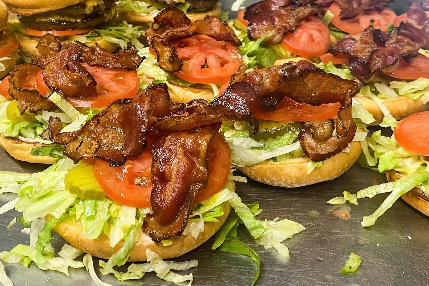 Open-faced sandwiches with lettuce, tomato, and crispy bacon on buns, arranged on a metal tray.