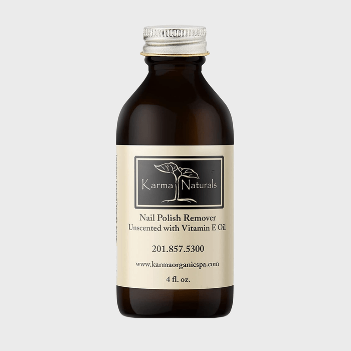 A brown bottle displays Karma Naturals nail polish remover label, featuring tree logo, unscented with Vitamin E oil, 4 fl. oz., website, and phone number.