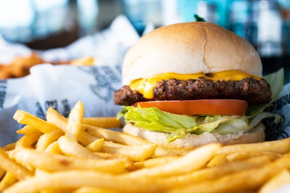 A cheeseburger sits on paper, surrounded by crispy fries in a dining setting.