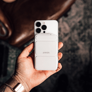 Hand holding a smartphone with an Anker accessory attached, on a blurred, textured background.
