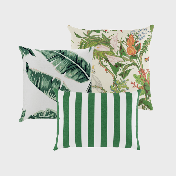 Three decorative pillows overlap; one features banana leaves, another showcases floral patterns, and the third displays green and white stripes, against a plain background.