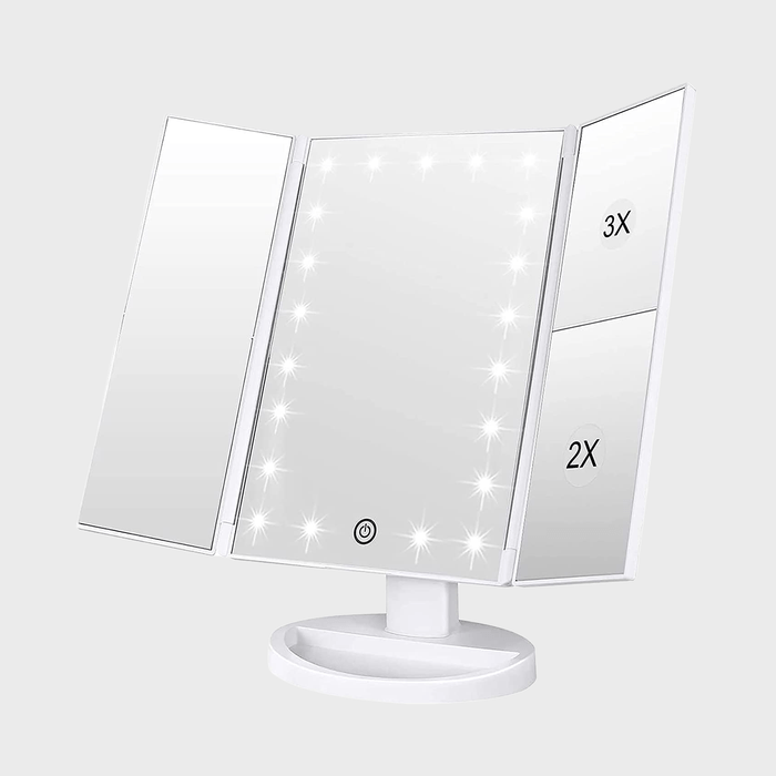 Tri-fold vanity mirror lights up with magnification (2X, 3X) on side panels, resting on a white base in a neutral setting.