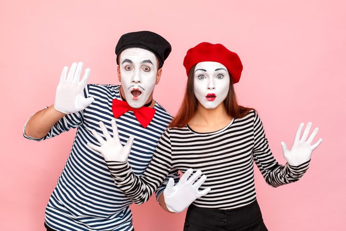 Two mimes with surprised expressions gesture dramatically against a pink background, wearing striped shirts, white gloves, and berets.