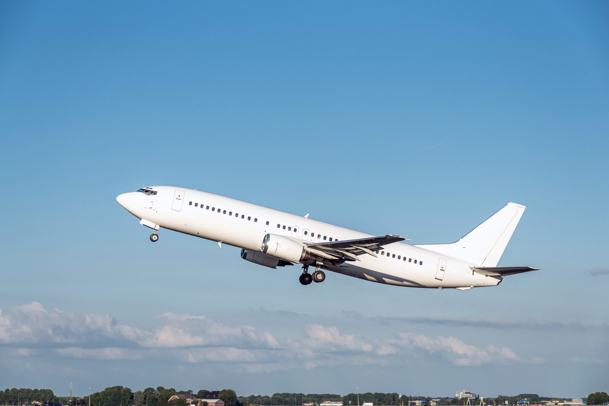 Airplane ascends, engines roaring, against a clear blue sky with clouds; landscape visible below in the background.