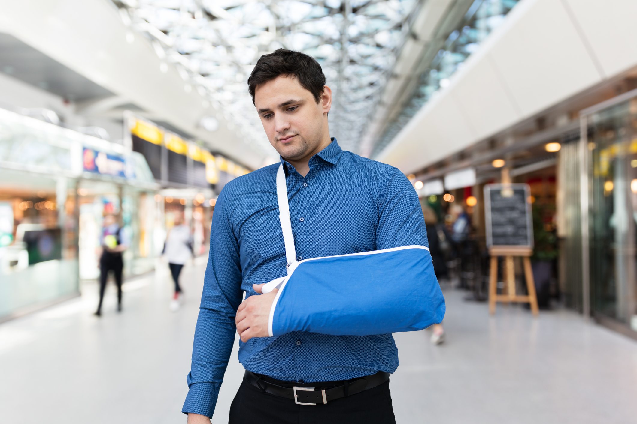 Man wears arm sling, walking in a bright, modern shopping mall.