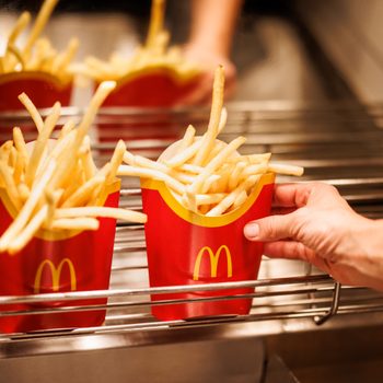 French fries in red containers being placed on a metal rack by a hand in a fast-food kitchen.