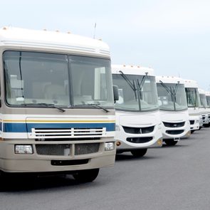 RVs parked in a row on an asphalt lot, aligned in a straight line, with a cloudy sky overhead.