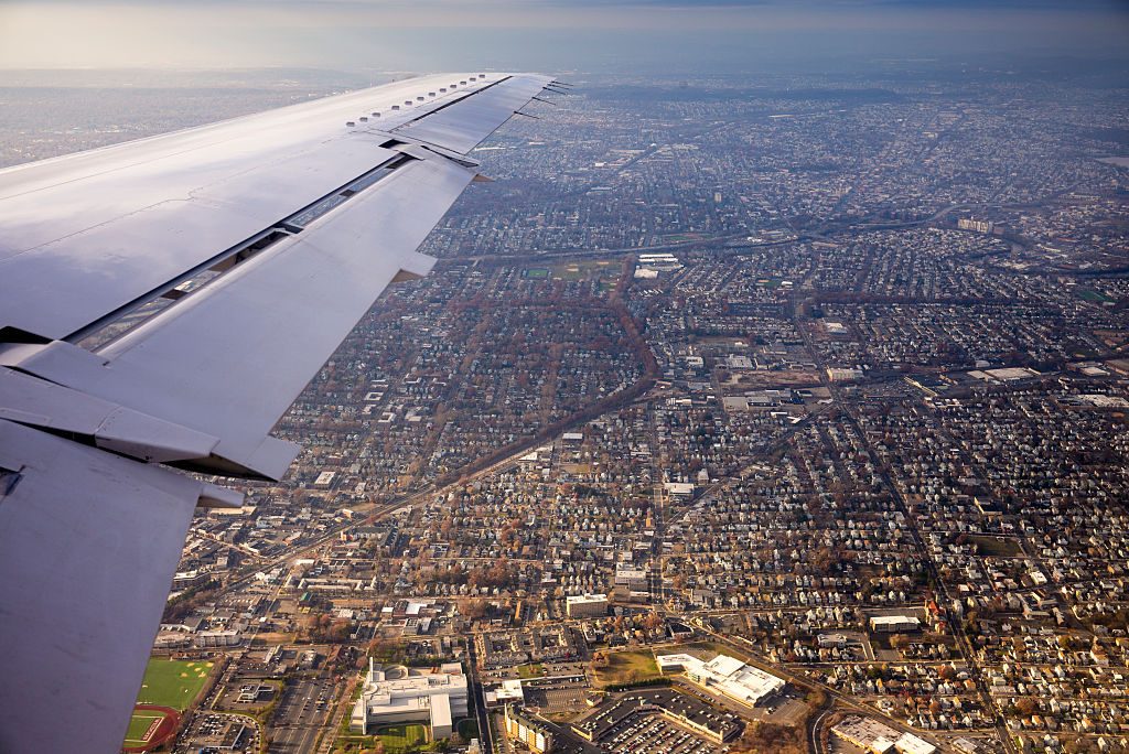 Airplane wing glides over a sprawling urban landscape, revealing a dense grid of buildings and roads under a clear sky.