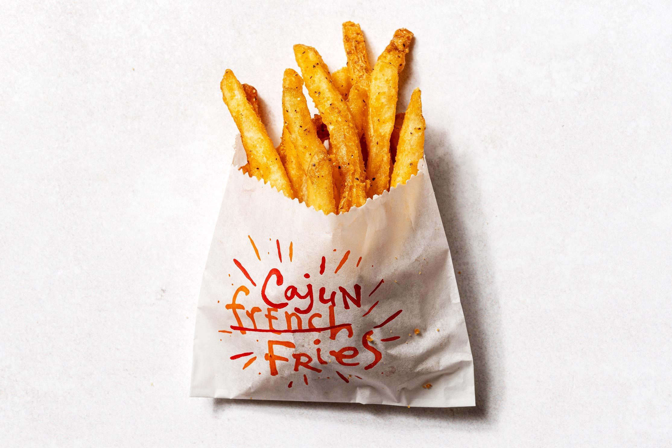 French fries, standing upright in a paper bag, are labeled "Cajun French Fries" with a light background.
