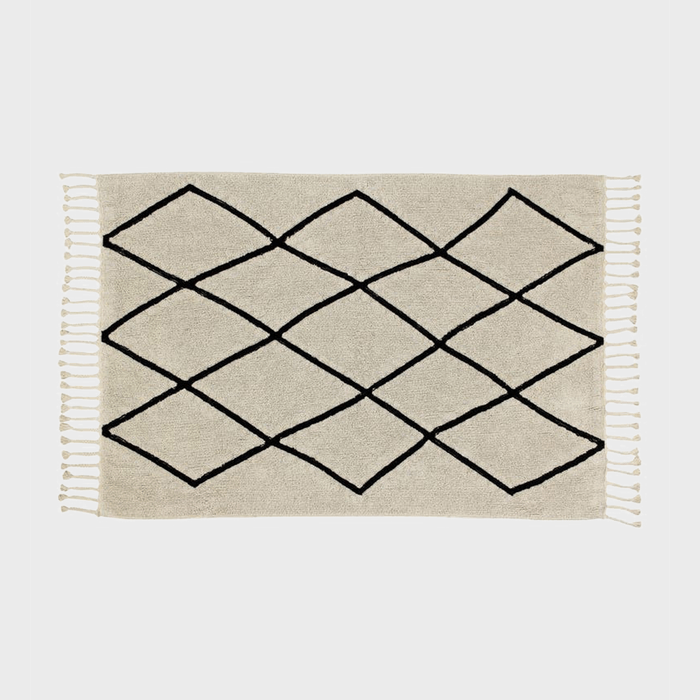 A beige rug displays a black geometric diamond pattern, set against a plain white background, with fringed edges.