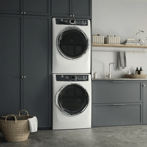Stacked washer and dryer units stand idle beside navy blue cabinets in a modern laundry room with gray floor tiles and a woven basket.