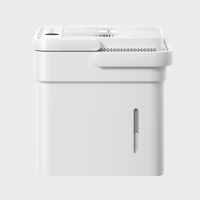 White air purifier sits in minimalist setting, featuring a top control panel and side air vent, against a light gray background.