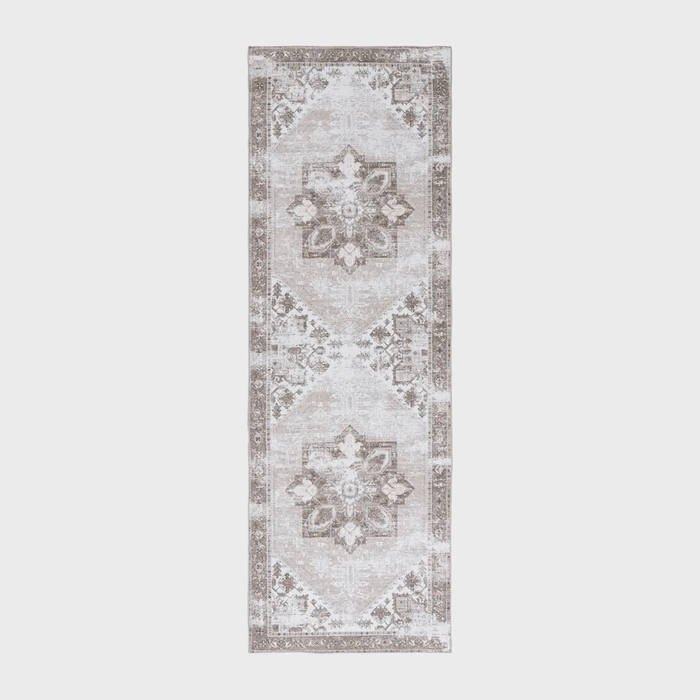 Rectangular rug displaying intricate geometric patterns in neutral tones, placed on a plain background.