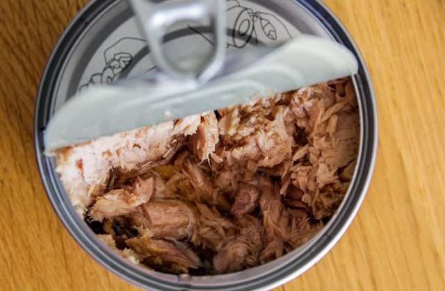 An open can of pink tuna chunks sits on a wooden table.