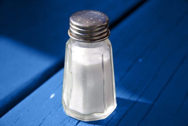 A salt shaker sits on a bright blue wooden surface, angled in natural sunlight.