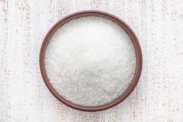 Bowl holding granulated white sugar, resting on a textured white surface.