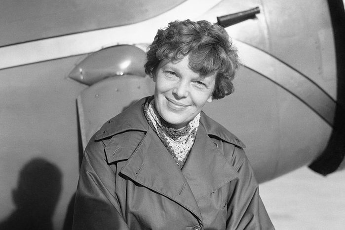 portrait of Amelia Earhart sitting outside in front of an airplane