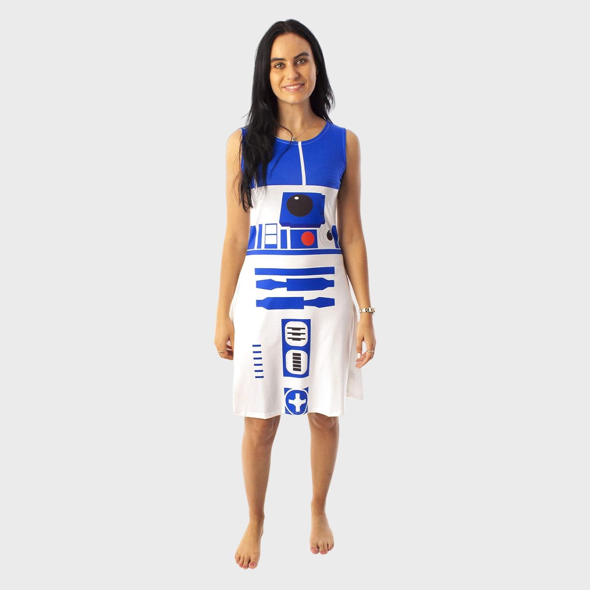 A person stands smiling, wearing a sleeveless dress resembling a droid design, on a plain gray background, barefoot.