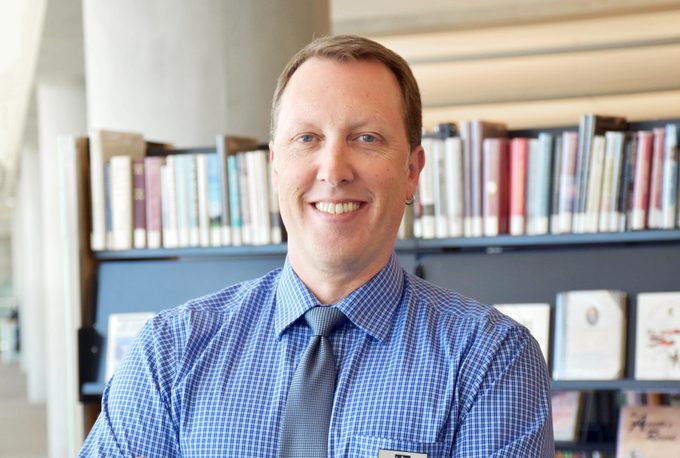 portrait of Peter Bromberg smiling with shelves of books behind him