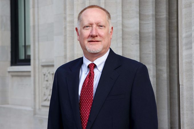 portrait of Lee Burchfield in a suit with a red tie standing outside in front of a building
