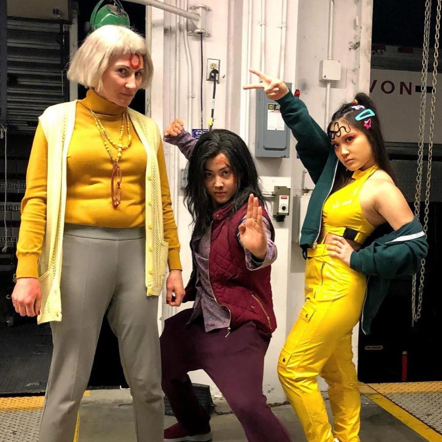 Three people pose playfully in colorful costumes inside a building, striking dynamic and confident gestures with playful expressions.