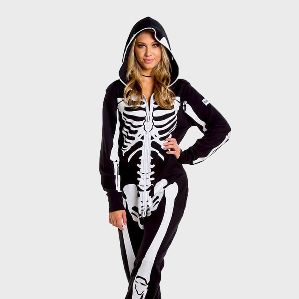 A person wears a hooded skeleton-print onesie, standing against a plain background with one hand on hip.