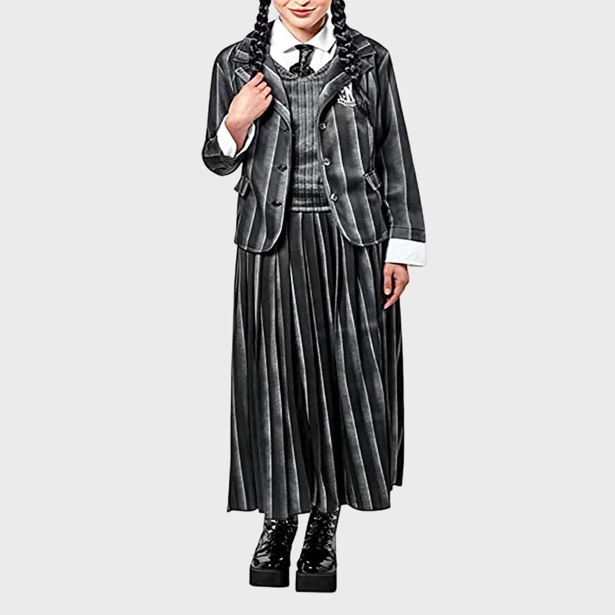 A person wears a pinstriped suit with a pleated skirt on a plain background, holding one hand to the lapel.