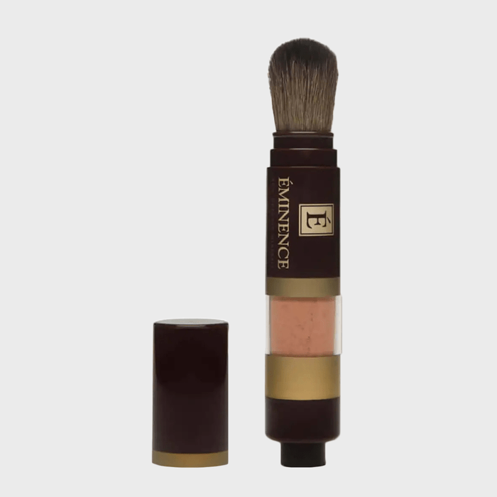 Brush dispenses product, standing upright; dark container with a visible section of loose powder. Marked with 