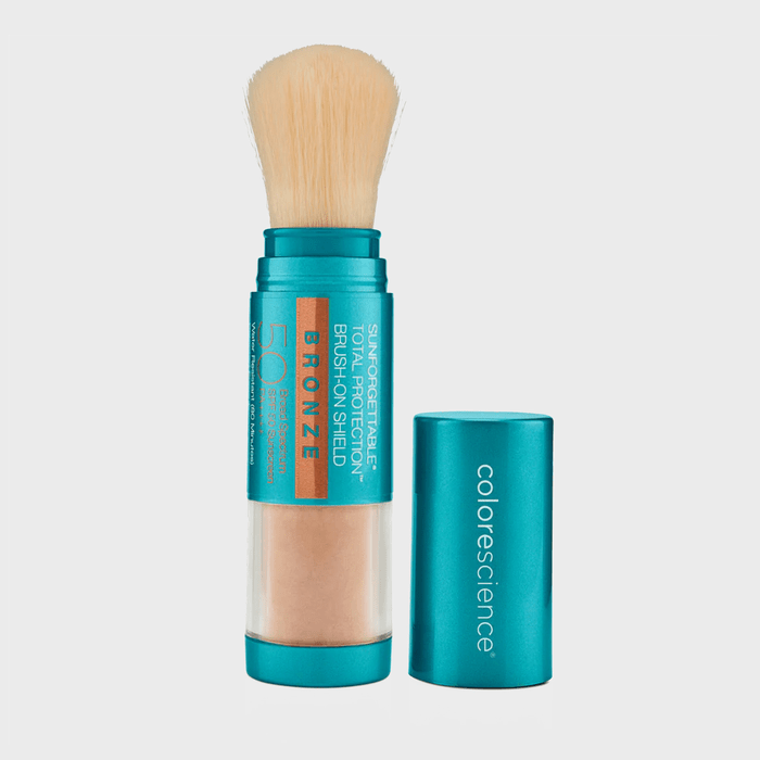 A makeup brush dispenses powder, held in a teal container labeled 
