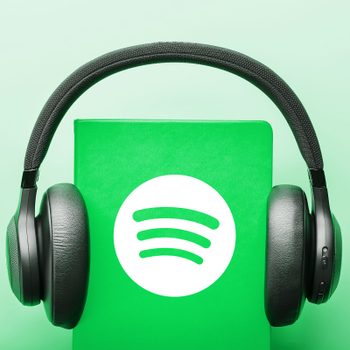 Headphones rest on a green notebook displaying the Spotify logo, set against a light green background.