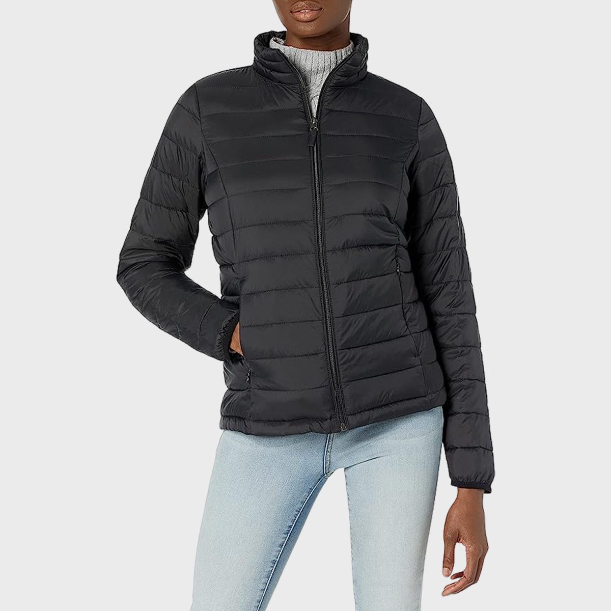 A person wears a black quilted jacket, standing with hands in jeans pockets against a plain background.