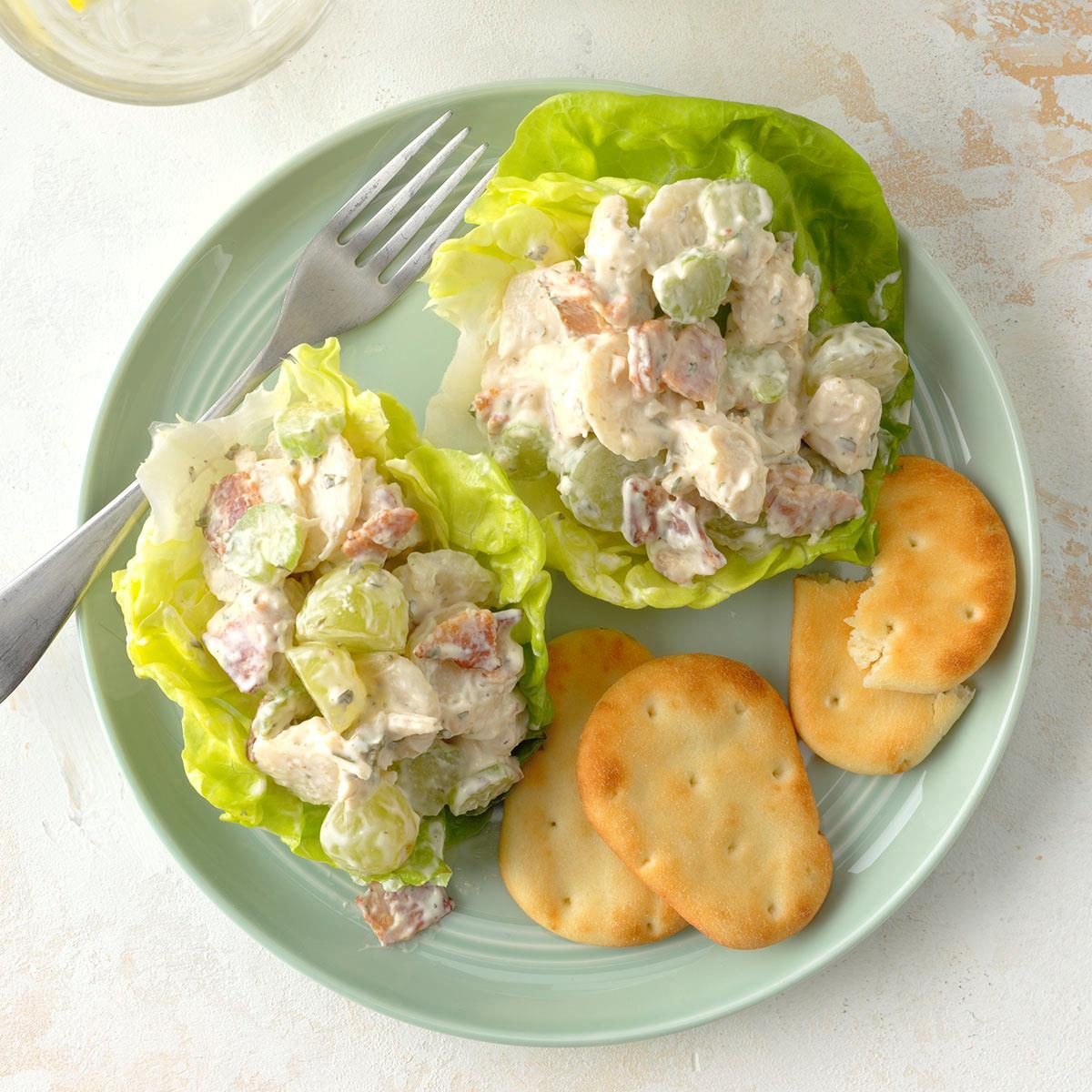 Lettuce cups filled with creamy chicken salad sit on a plate with crackers and a fork, placed on a light-colored surface.