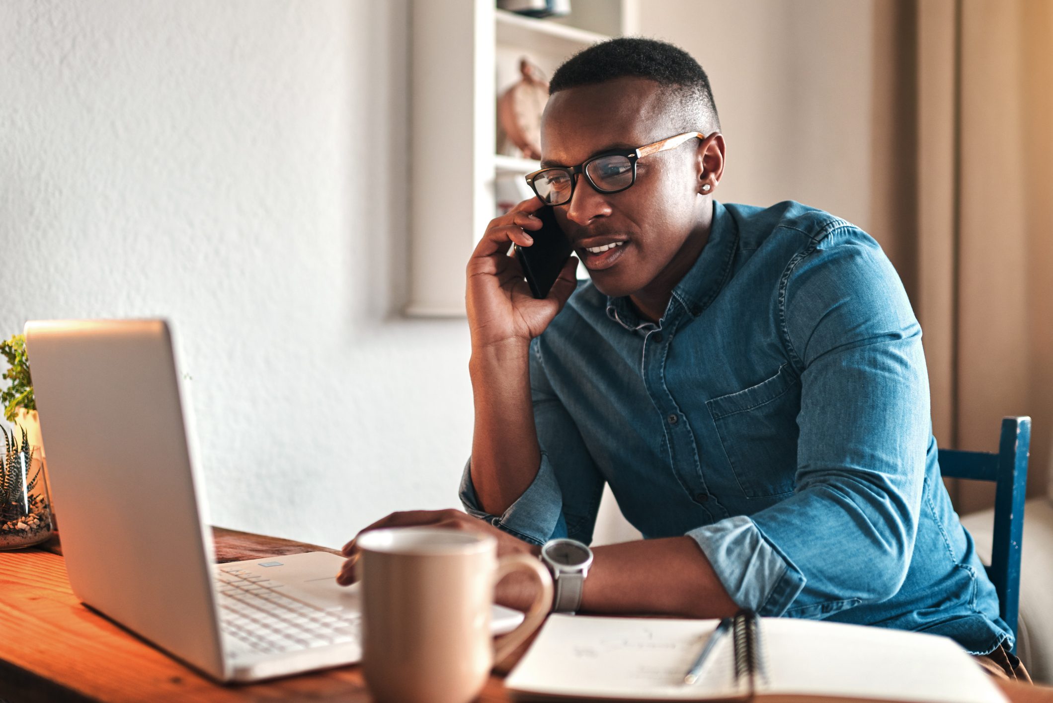young businessman sitting alone in his home office and talking on his cellphone