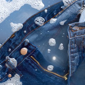 Denim jeans submerged in soapy water, surrounded by bubbles and foam, create a washing effect.